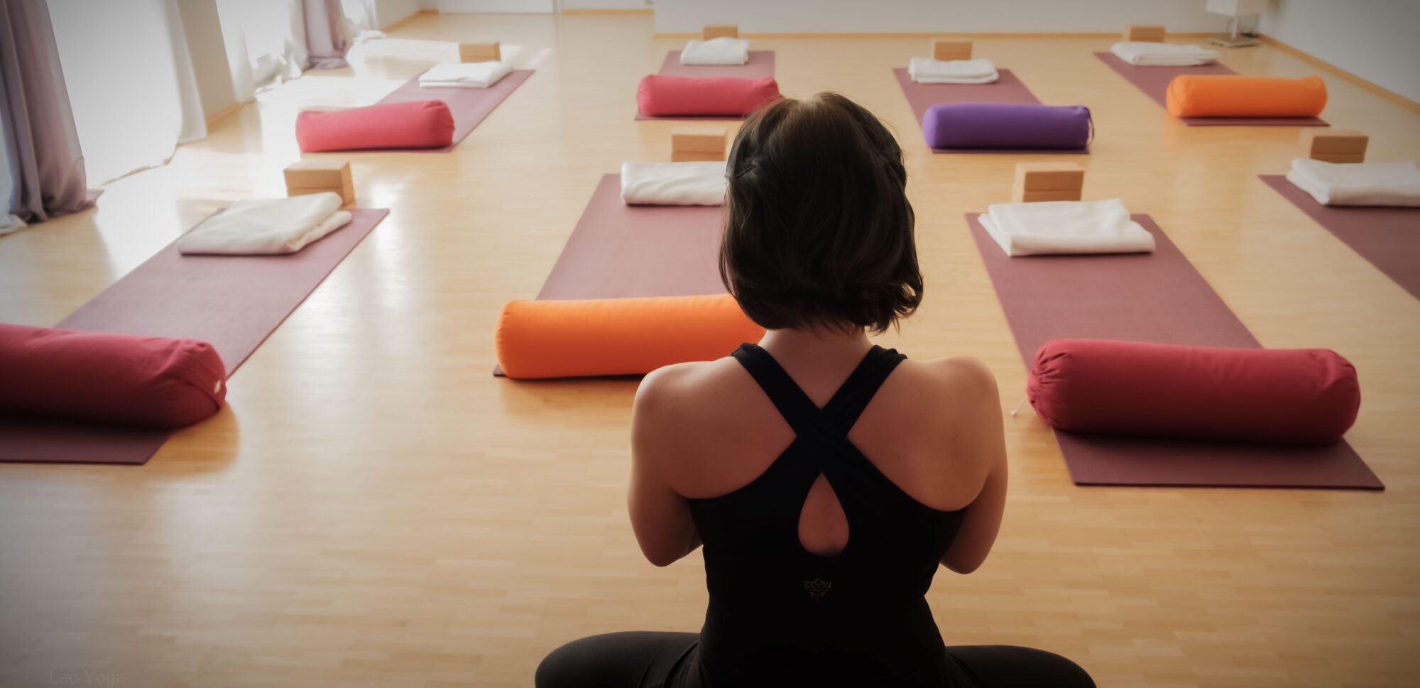 Leonie sitzt im meditaiv Schneidersitz auf der Matte, Ihr Blick geht in den Raum.